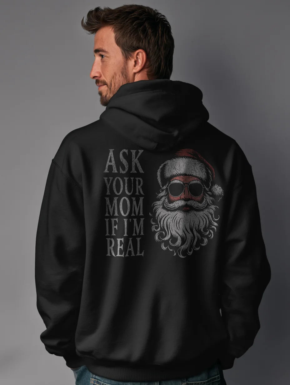 Black men’s hoodie with large vintage Santa face and sunglasses graphic on the back and distressed text that reads “Ask Your Mom If I’m Real,” modeled by a man standing in a studio with a gray background.