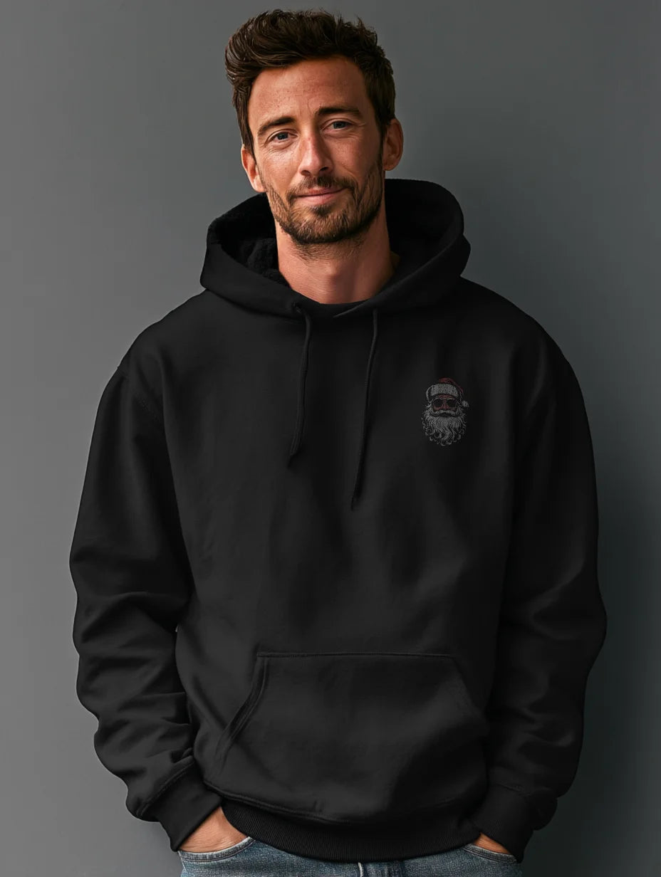 Black men’s hoodie with small vintage Santa face and sunglasses chest print, modeled by a man standing in a studio with a gray background, hands in the front pocket.