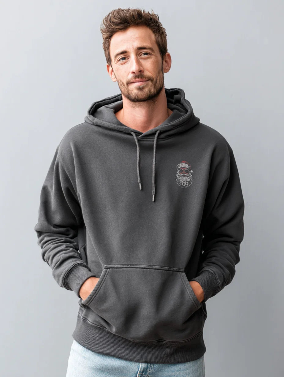 Charcoal men’s hoodie with small vintage Santa face and sunglasses chest print, modeled by a man standing in a studio with a gray background, hands in the front pocket.