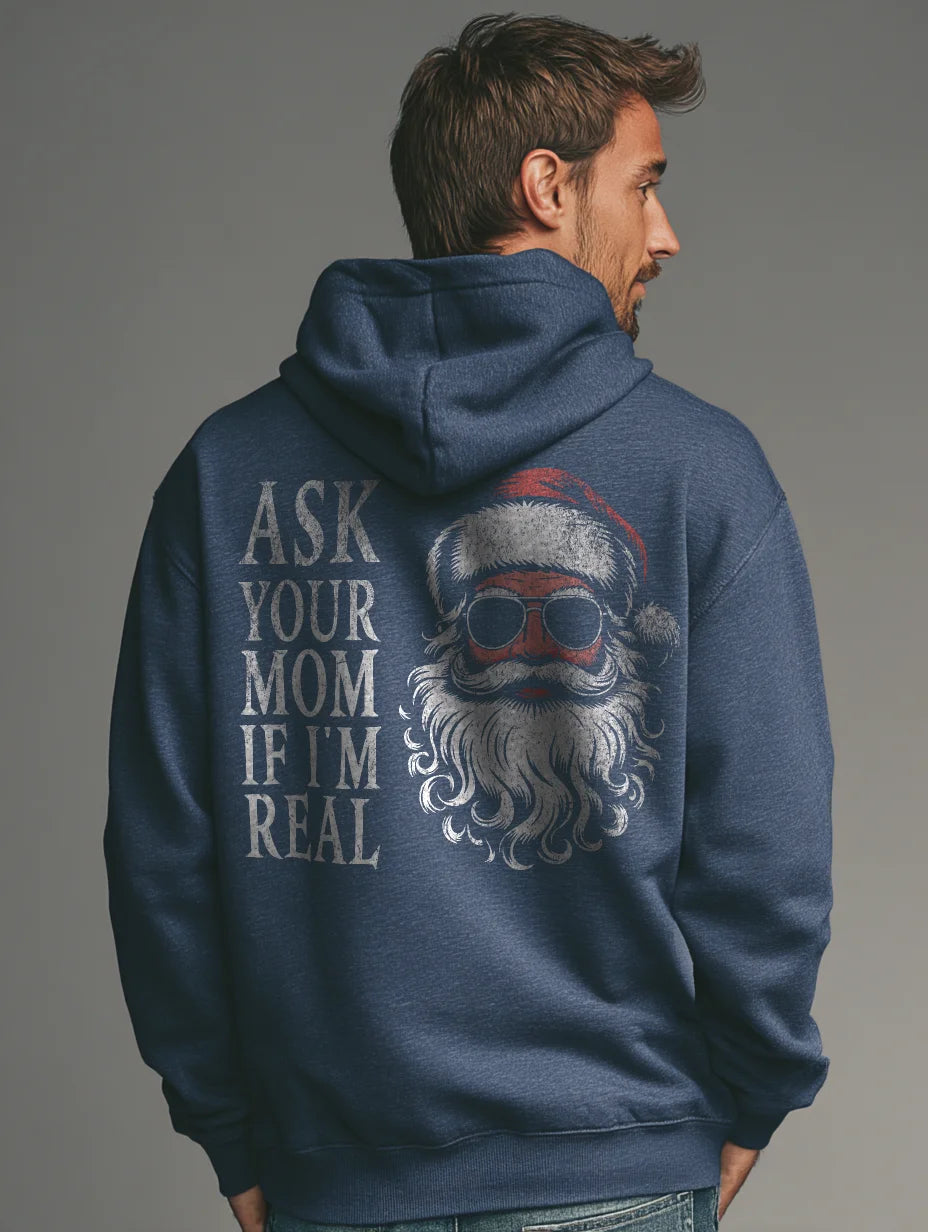 Heather Navy men’s hoodie with large vintage Santa face and sunglasses graphic on the back and distressed text that reads “Ask Your Mom If I’m Real,” modeled by a man standing in a studio with a gray background.
