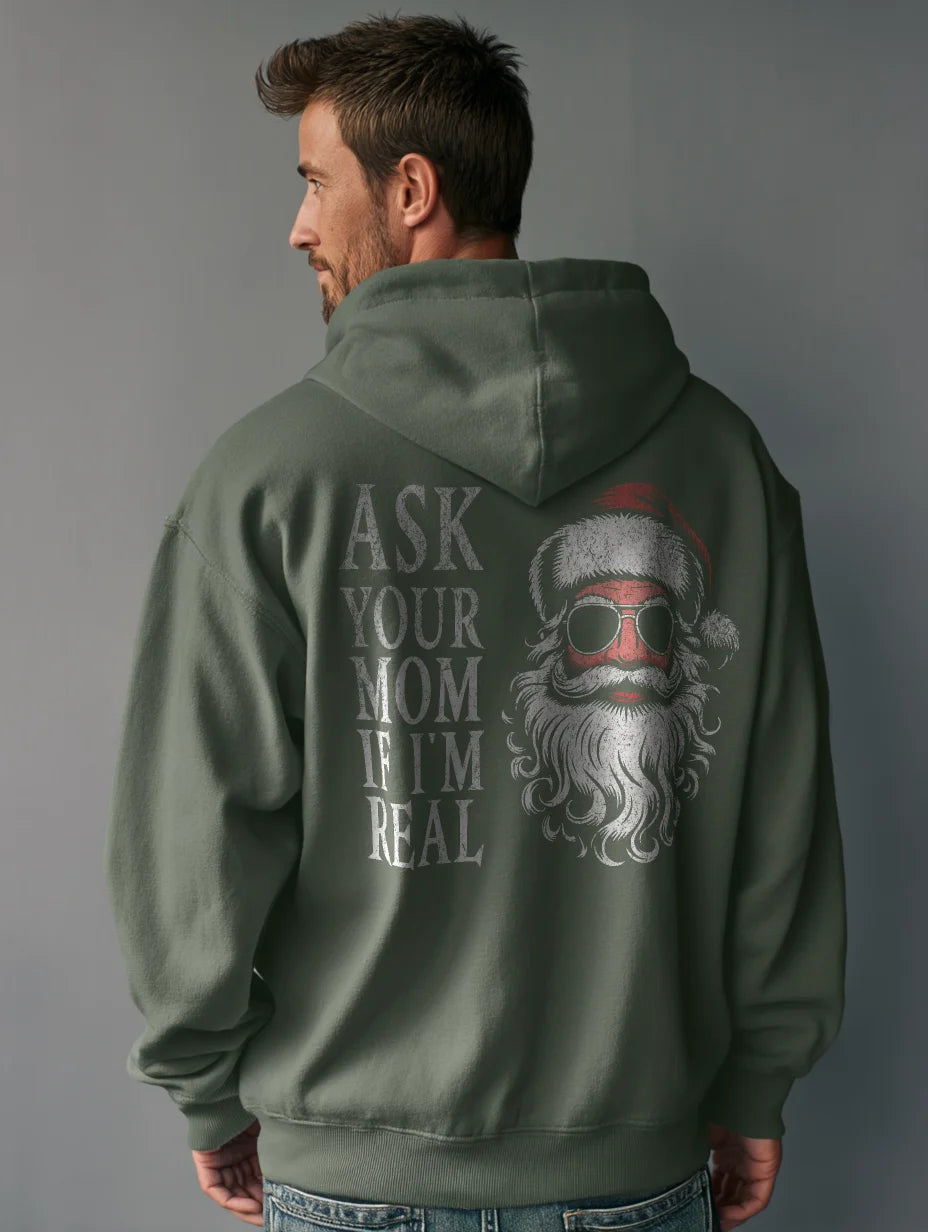 Military Green men’s hoodie with large vintage Santa face and sunglasses graphic on the back and distressed text that reads “Ask Your Mom If I’m Real,” modeled by a man standing in a studio with a gray background.