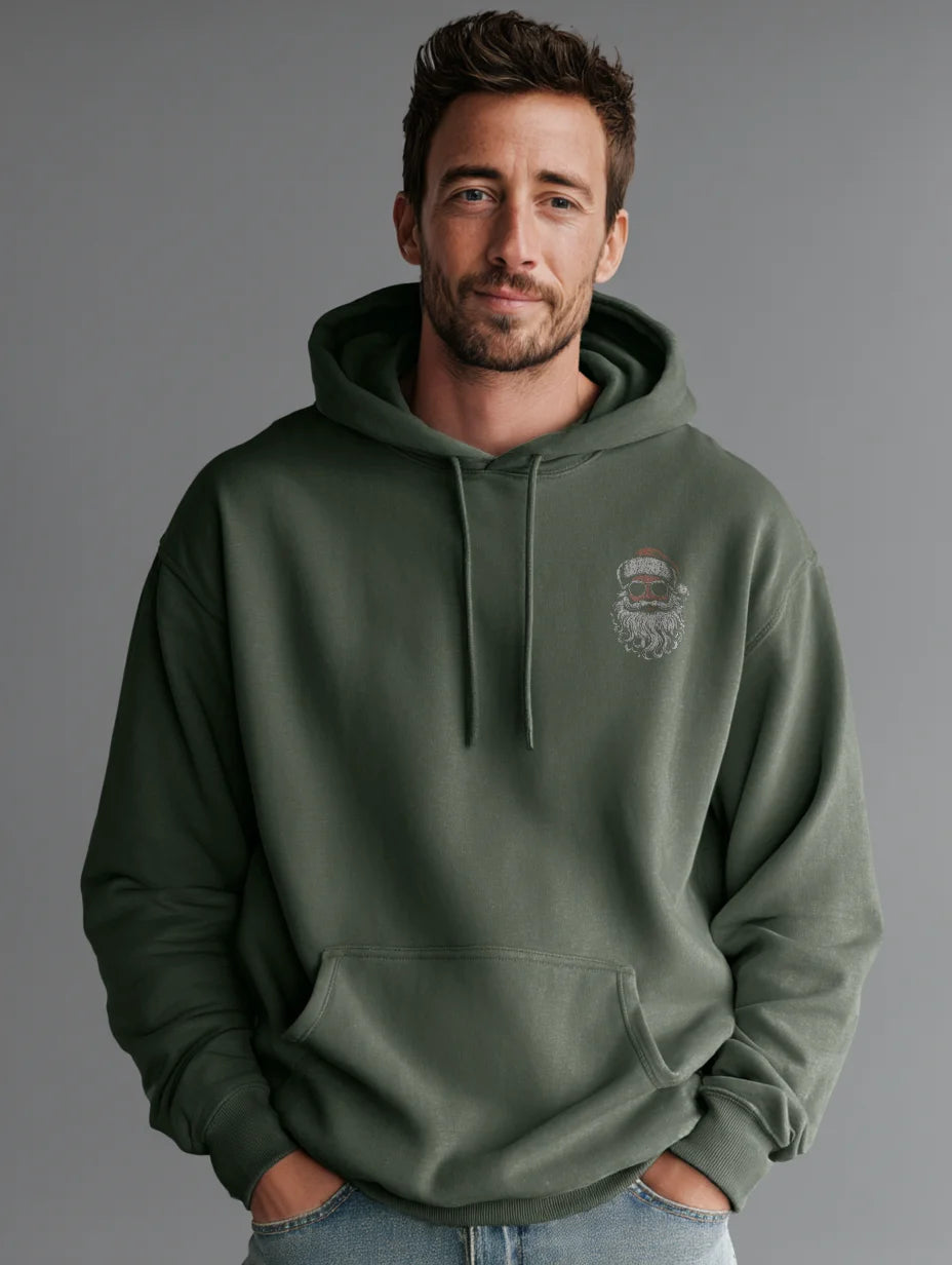 Military Green men’s hoodie with small vintage Santa face and sunglasses chest print, modeled by a man standing in a studio with a gray background, hands in the front pocket.