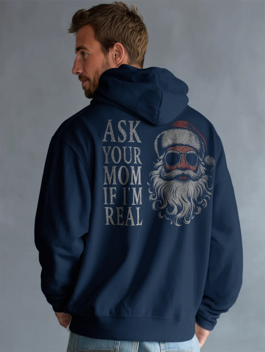 Navy men’s hoodie with large vintage Santa face and sunglasses graphic on the back and distressed text that reads “Ask Your Mom If I’m Real,” modeled by a man standing in a studio with a gray background.