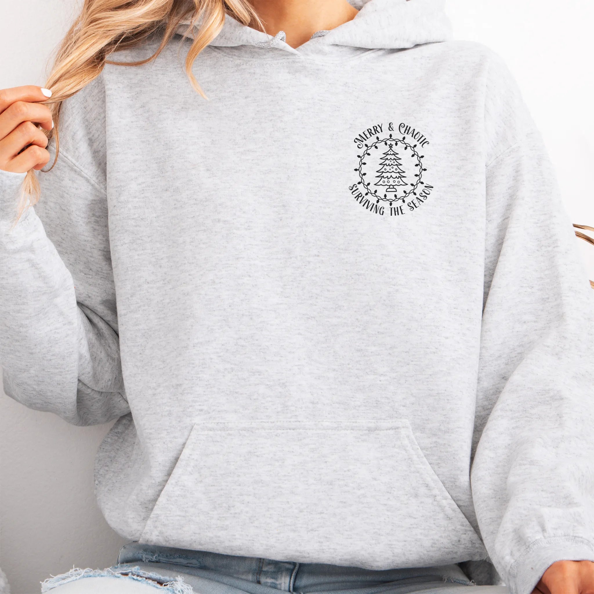 Ash women’s hoodie left chest badge text “Merry & Chaotic — Surviving the Season”