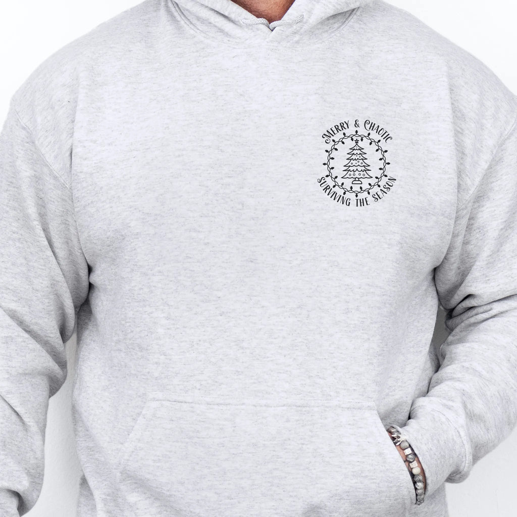 Ash men’s hoodie left chest badge text “Merry & Chaotic — Surviving the Season”