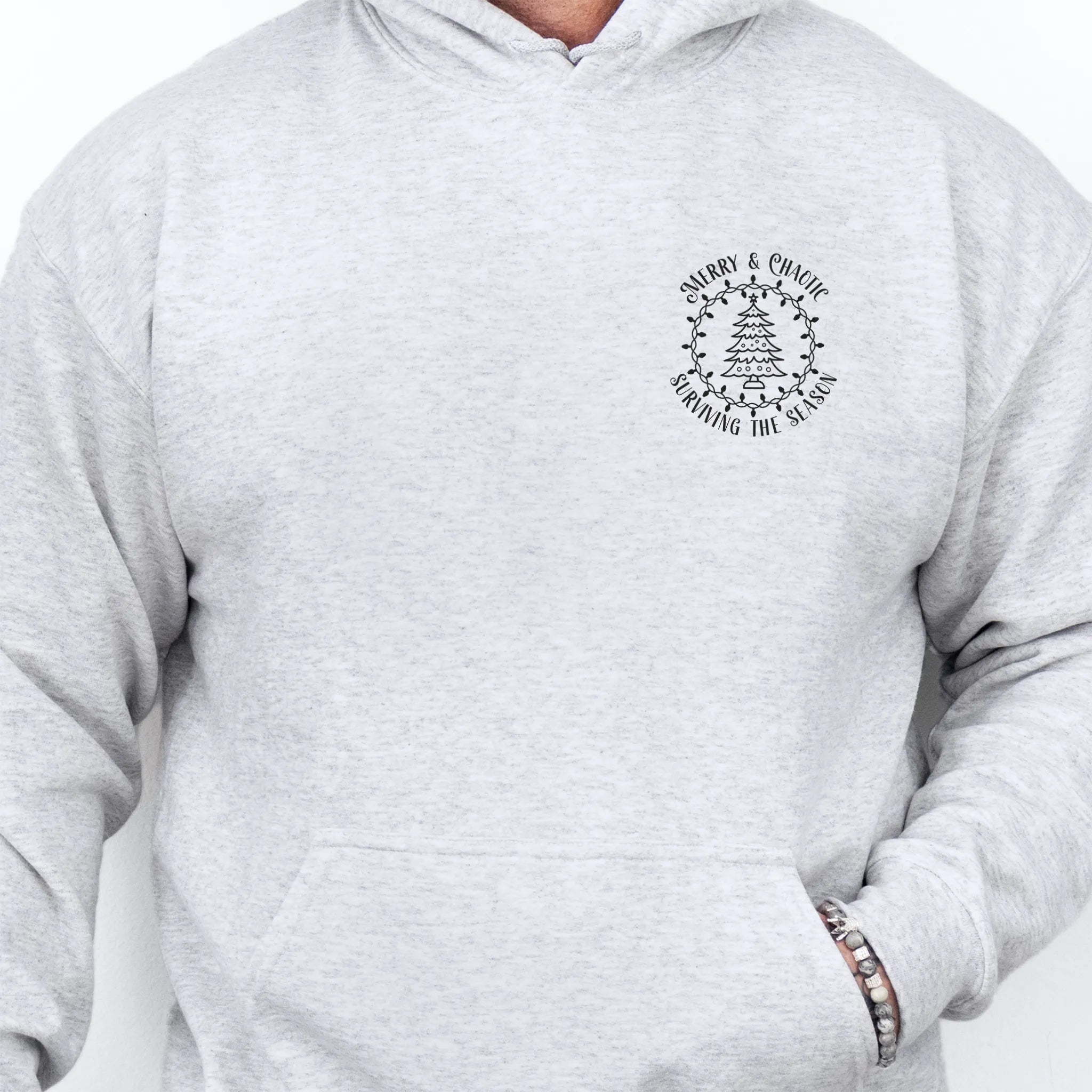 Ash men’s hoodie left chest badge text “Merry & Chaotic — Surviving the Season”