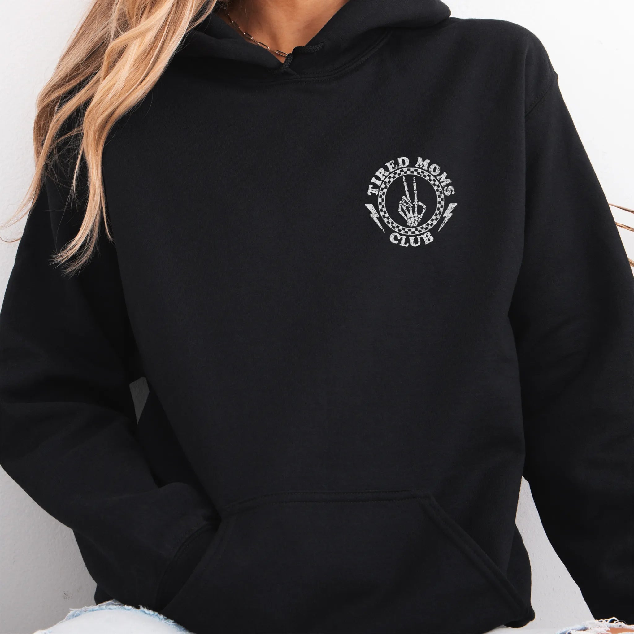 Black Oakley June Hoodie front view small left chest Tired Moms Club badge crest kangaroo pocket drawstrings visible distressed print