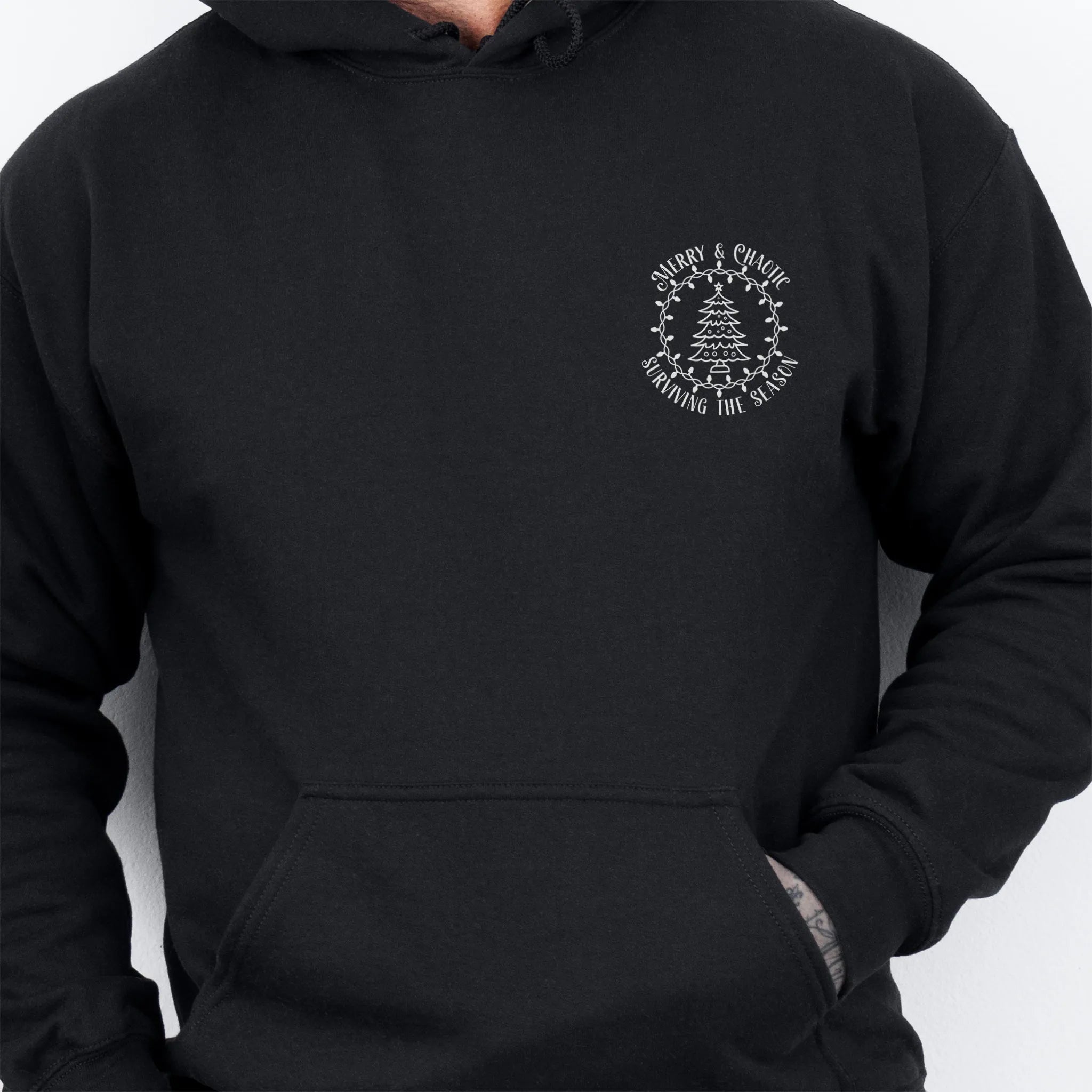 Black men’s hoodie left chest badge text “Merry & Chaotic — Surviving the Season”