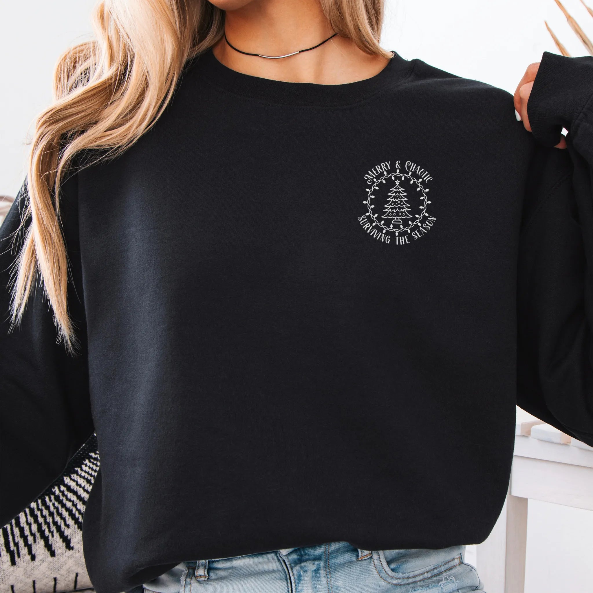 Black women’s sweatshirt left chest badge text “Merry & Chaotic — Surviving the Season”