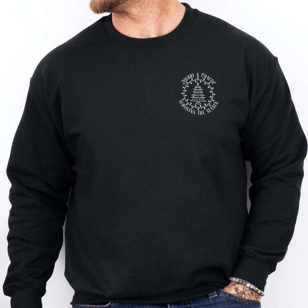 Black men’s sweatshirt left chest badge text “Merry & Chaotic — Surviving the Season”