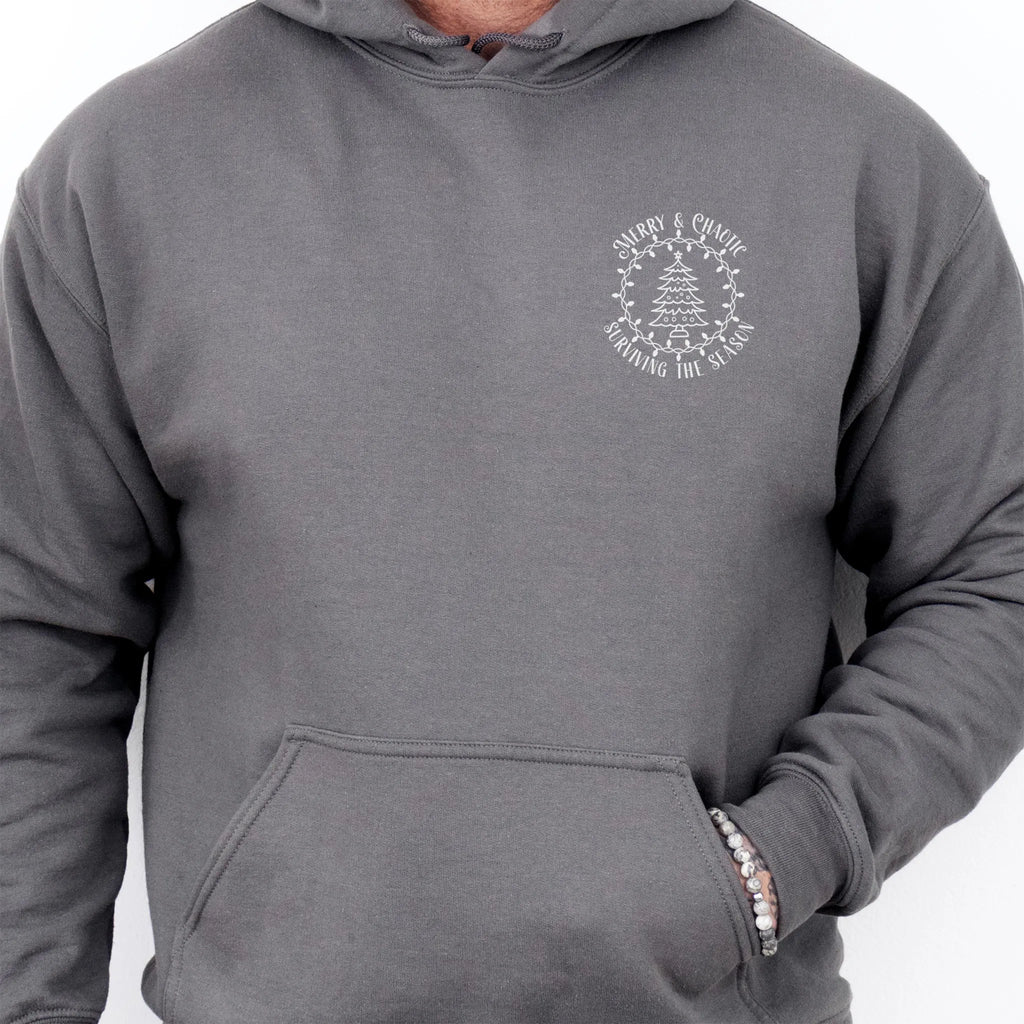 Charcoal men’s hoodie left chest badge text “Merry & Chaotic — Surviving the Season”