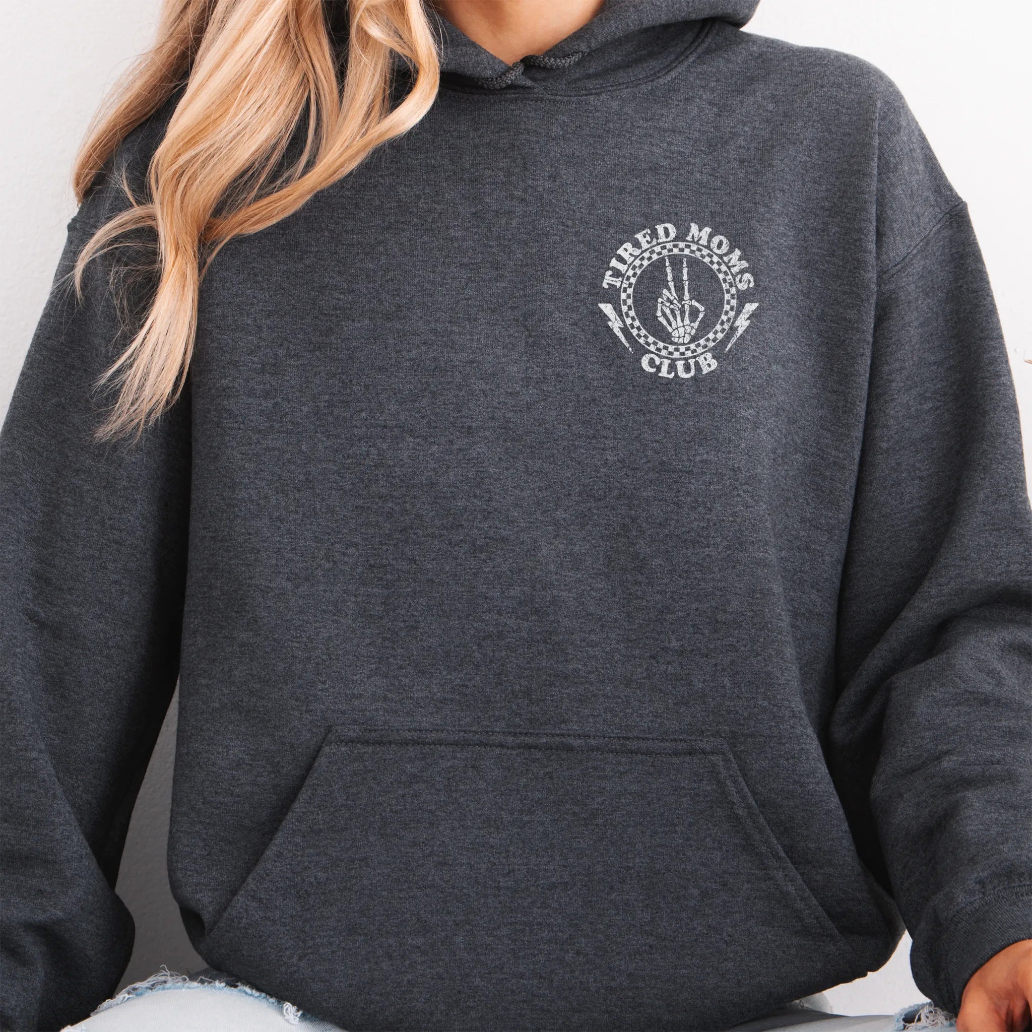 Dark Heather Oakley June Hoodie front view small left chest Tired Moms Club badge crest kangaroo pocket drawstrings visible distressed print