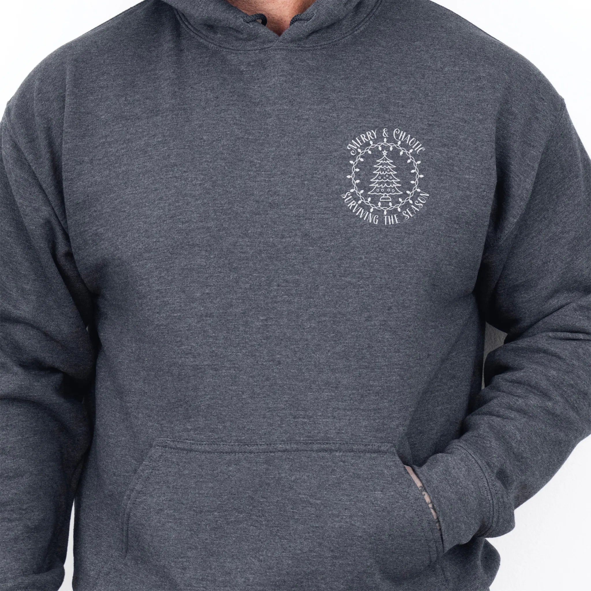 Dark Heather men’s hoodie left chest badge text “Merry & Chaotic — Surviving the Season”