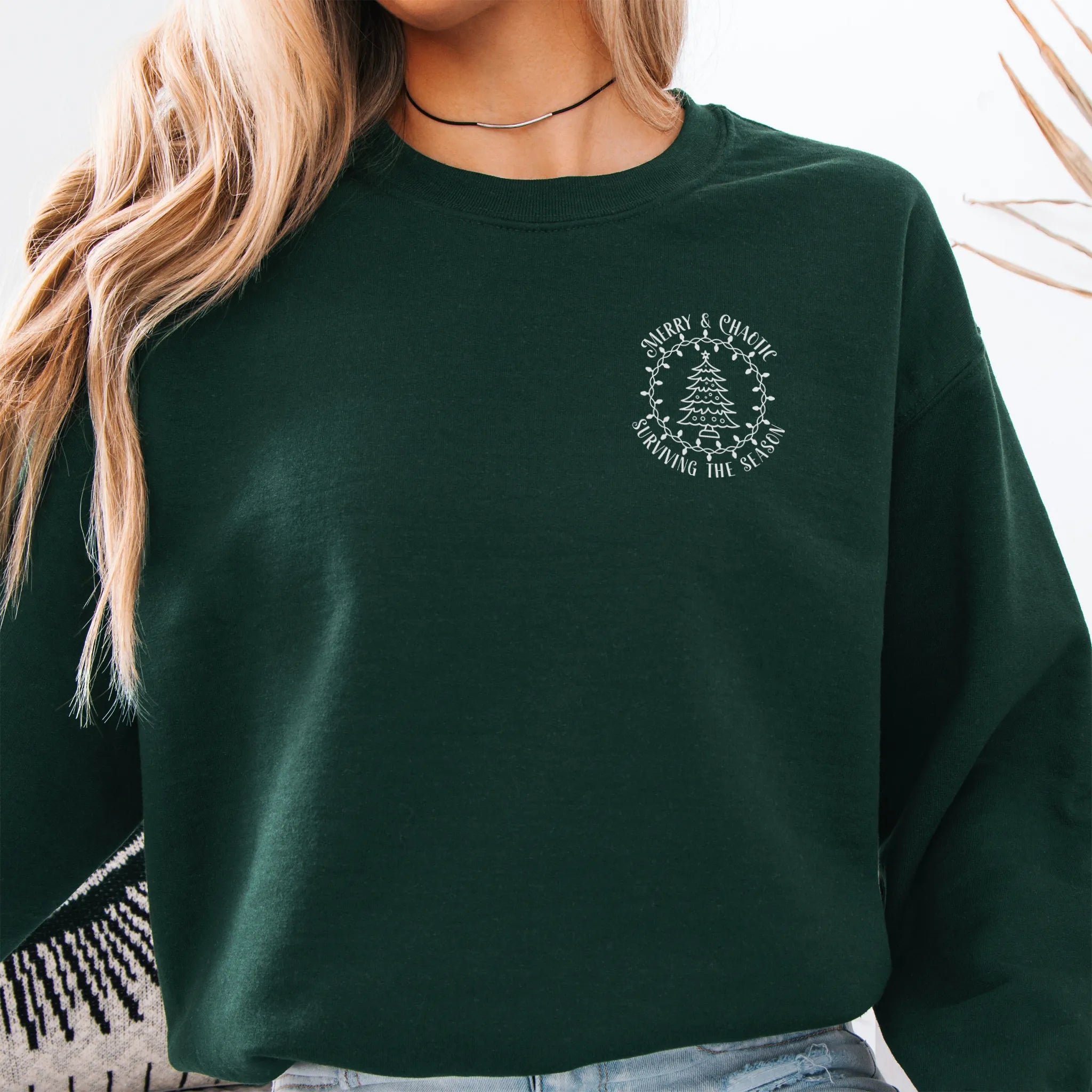 Forest Green women’s sweatshirt left chest badge text “Merry & Chaotic — Surviving the Season”