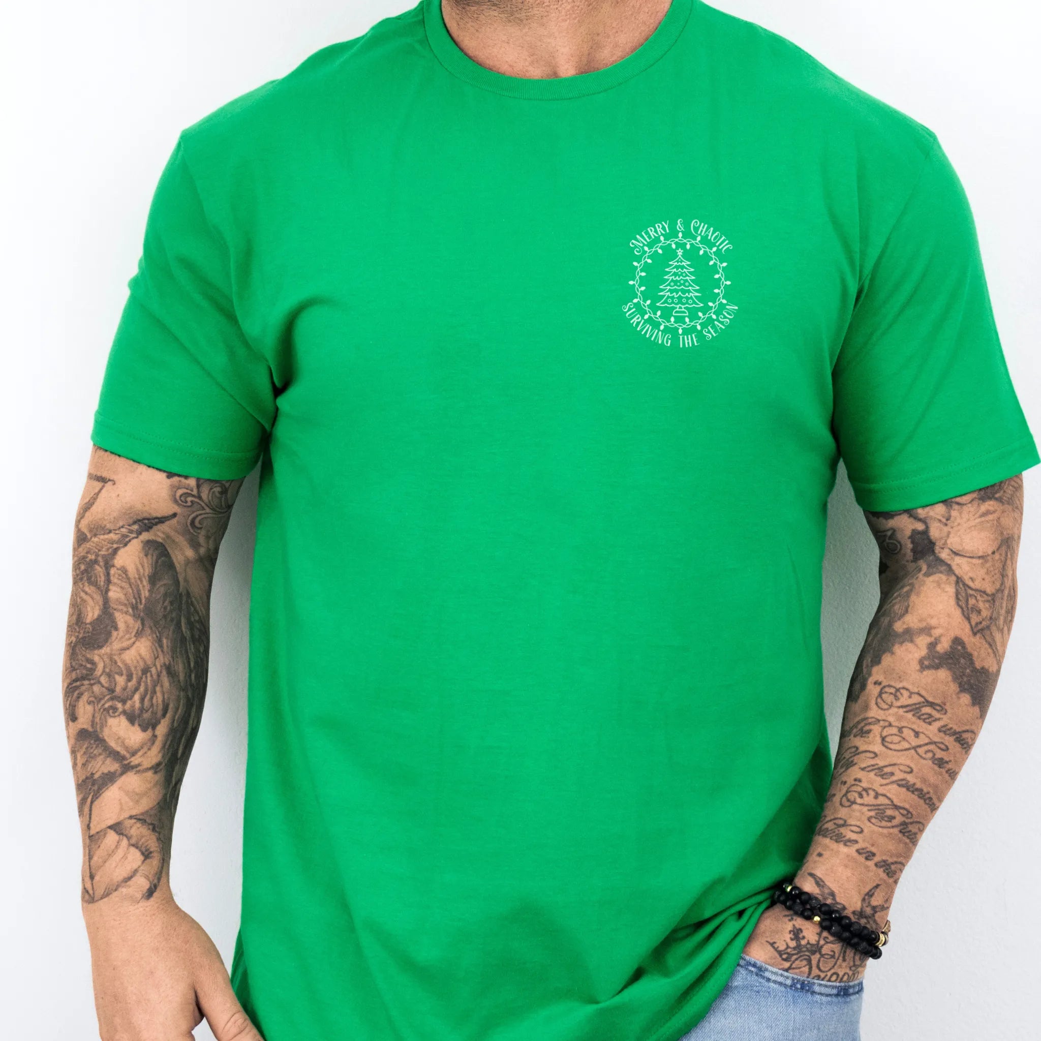 Irish Green Oakley June tee left chest badge text “Merry & Chaotic — Surviving the Season” with Christmas tree