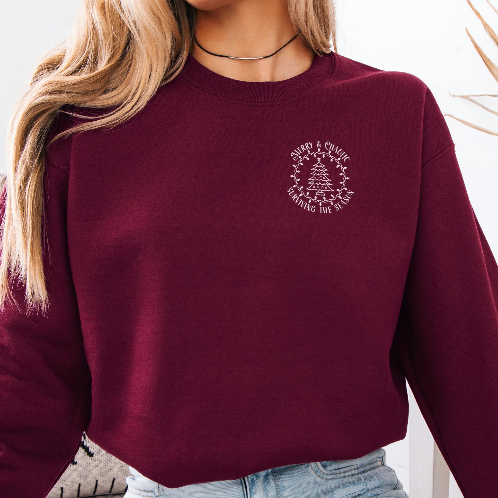 Maroon women’s sweatshirt left chest badge text “Merry & Chaotic — Surviving the Season”