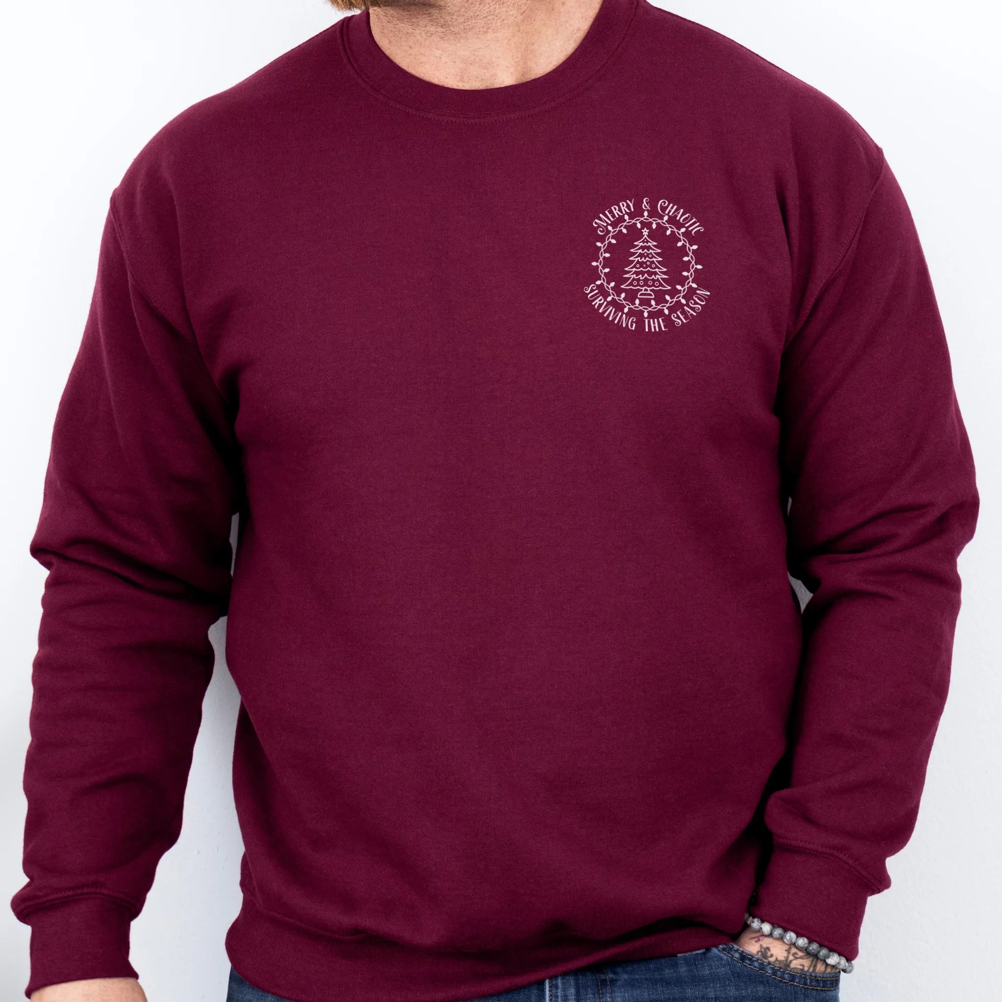 Maroon men’s sweatshirt left chest badge text “Merry & Chaotic — Surviving the Season”