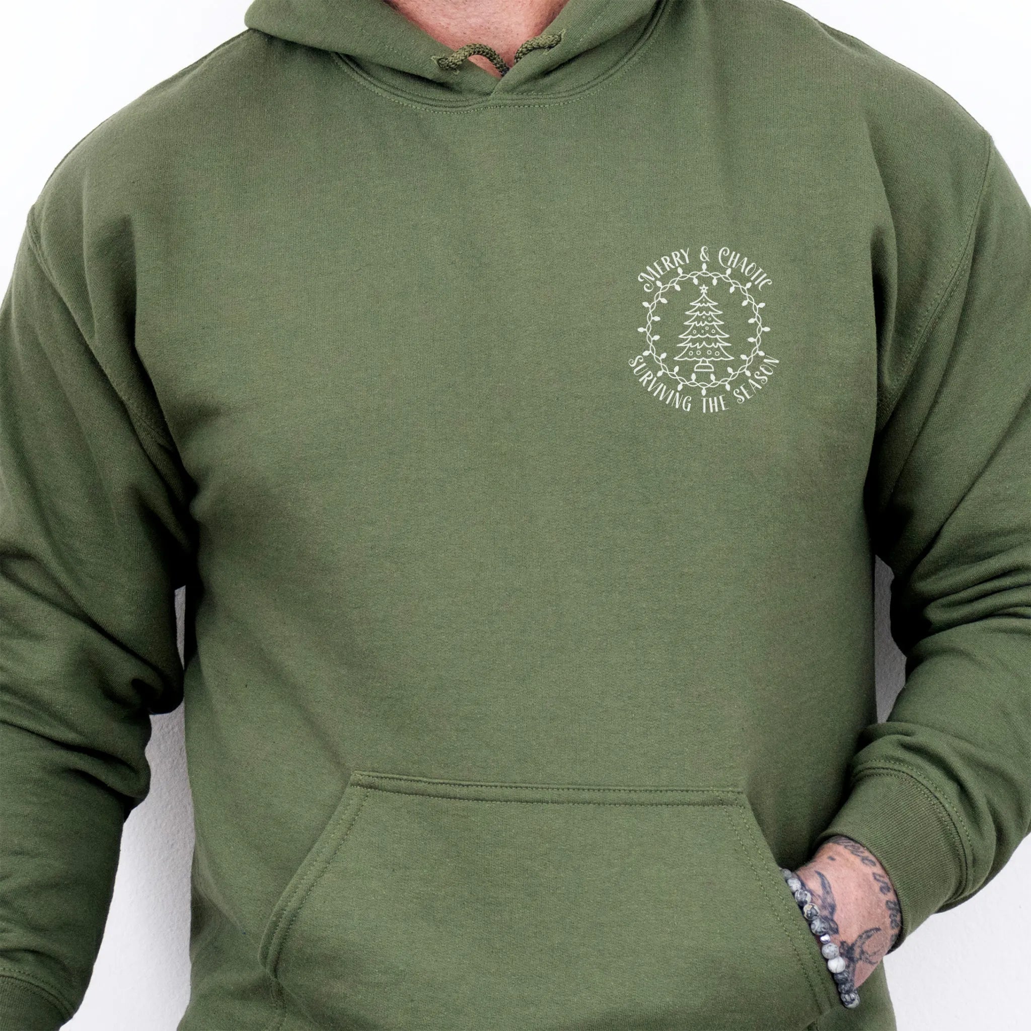 Military Green men’s hoodie left chest badge text “Merry & Chaotic — Surviving the Season”