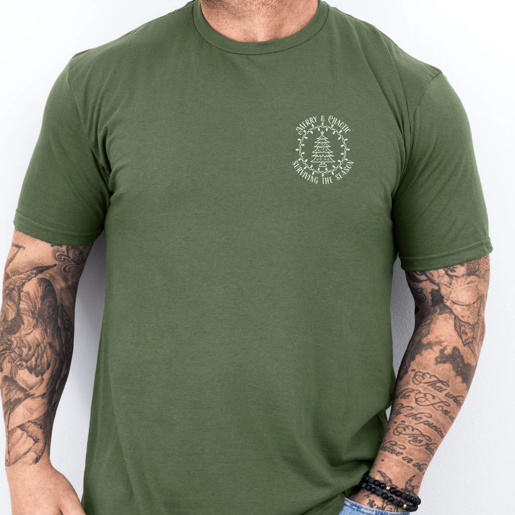 Military Green Oakley June tee left chest badge text “Merry & Chaotic — Surviving the Season” with Christmas tree