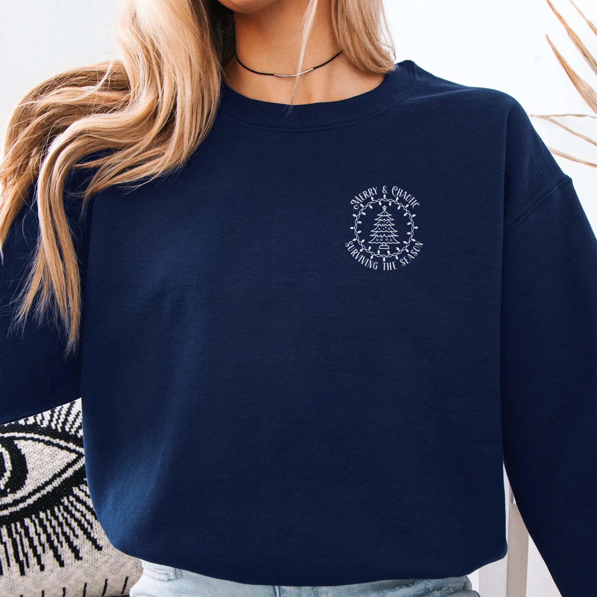 Navy women’s sweatshirt left chest badge text “Merry & Chaotic — Surviving the Season”