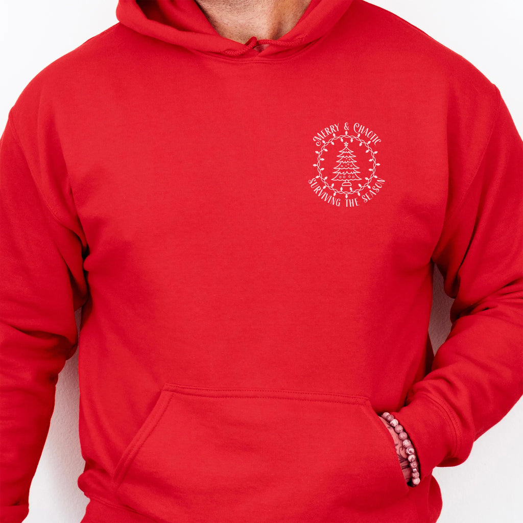 Red men’s hoodie left chest badge text “Merry & Chaotic — Surviving the Season”