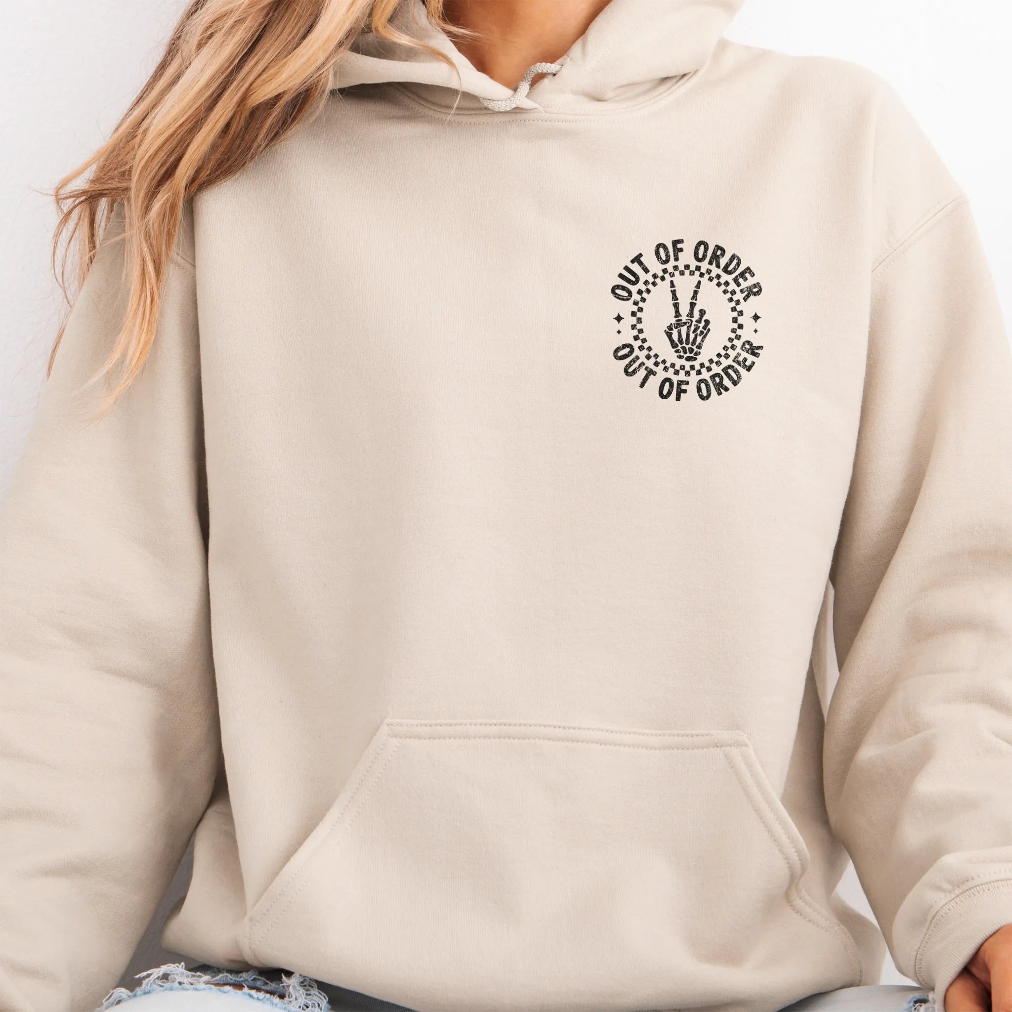 Sand hoodie – left chest circular badge with “Out of Order” text, kangaroo pocket and relaxed modern fit, studio front view