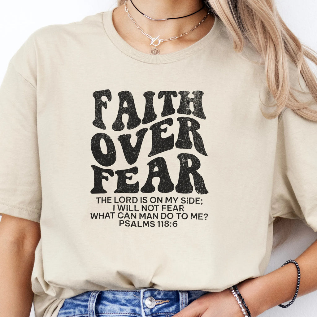 Sand Oakley June t shirt, large front lettering reads Faith Over Fear with supporting lines The Lord Is On My Side I Will Not Fear What Can Man Do To Me, studio front view