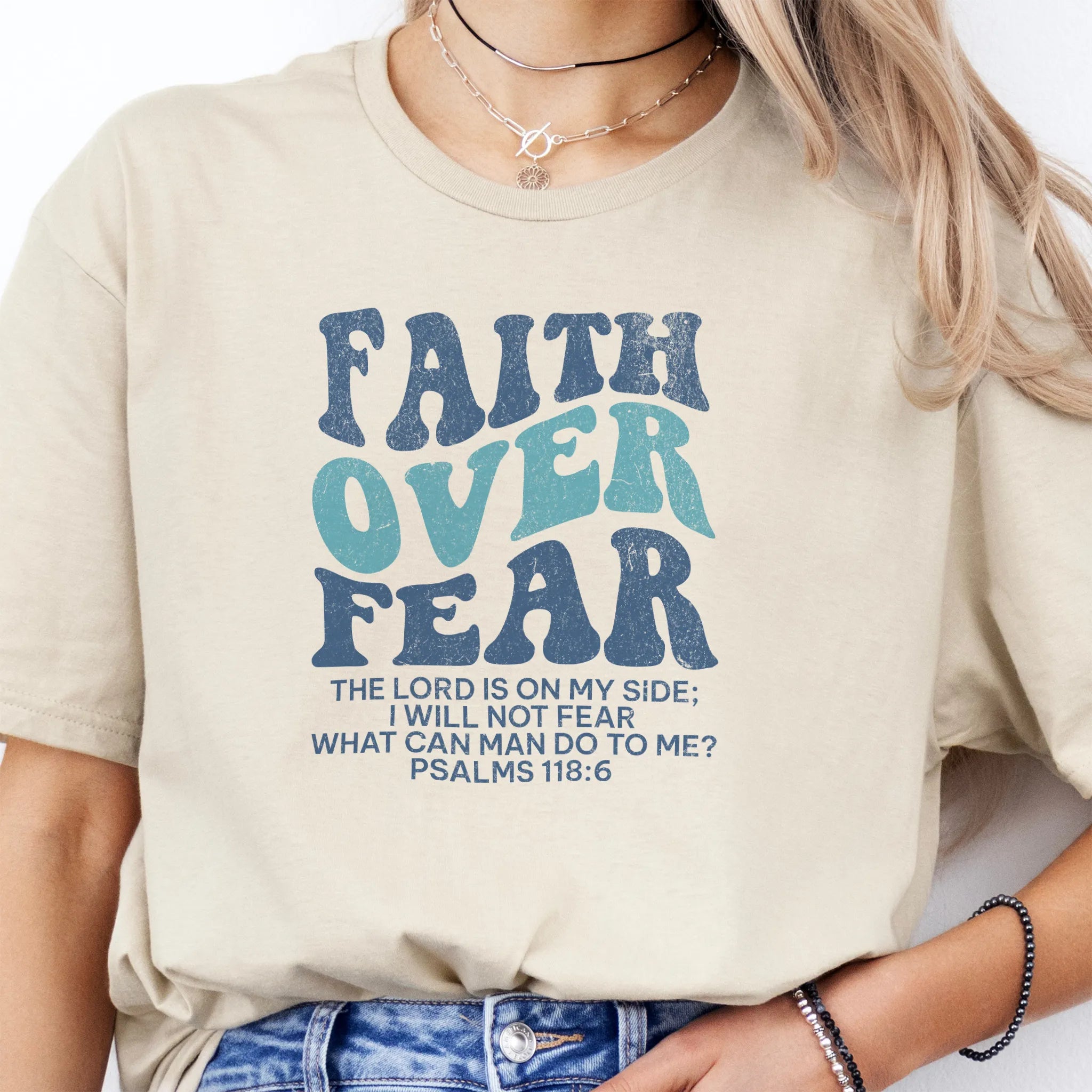 Sand Oakley June t shirt, large front lettering reads Faith Over Fear with supporting lines The Lord Is On My Side I Will Not Fear What Can Man Do To Me, studio front view