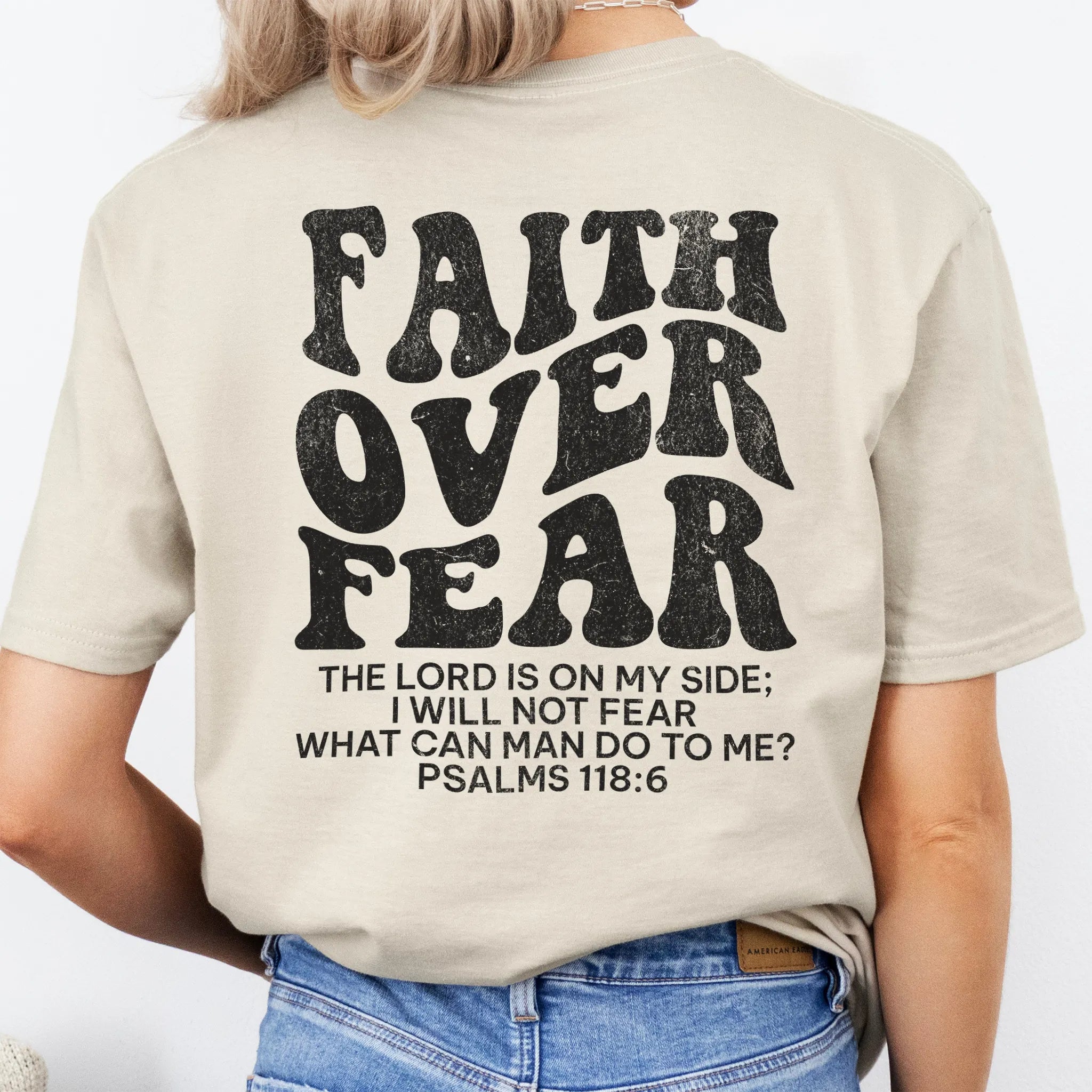 Sand Oakley June t shirt, large back lettering reads Faith Over Fear with supporting scripture reference Psalms one eighteen six, studio back view