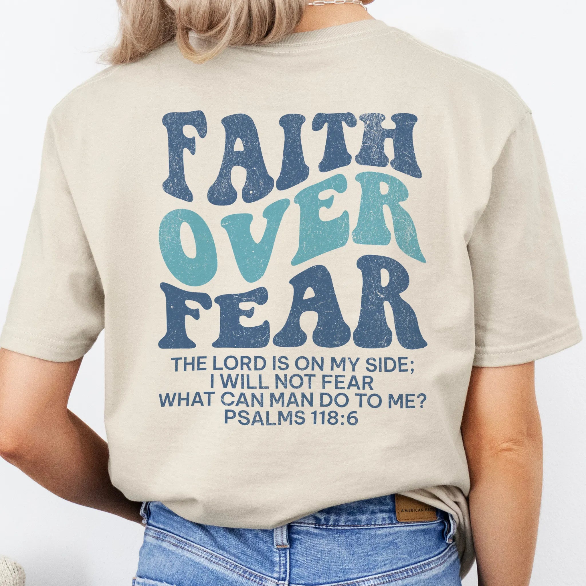 Sand Oakley June t shirt, large back lettering reads Faith Over Fear with supporting scripture lines, studio back view