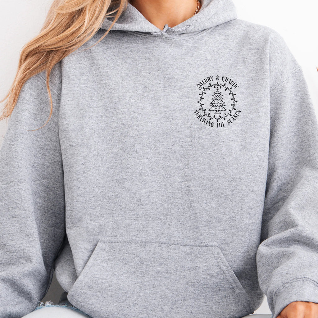 Sport Grey women’s hoodie left chest badge text “Merry & Chaotic — Surviving the Season”